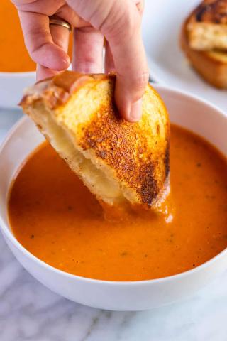 picture of a hand dipping grilled cheese into tomato soup